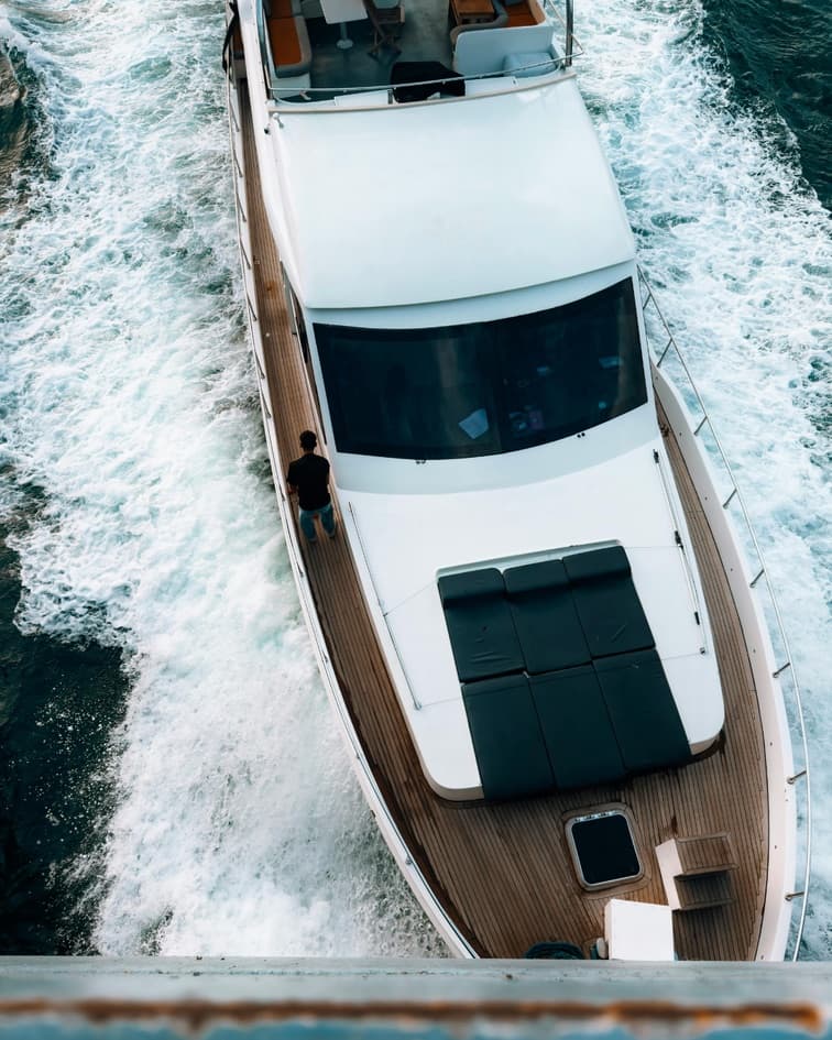 Aerial photograph of a motor yacht cutting a white wake across teal water.